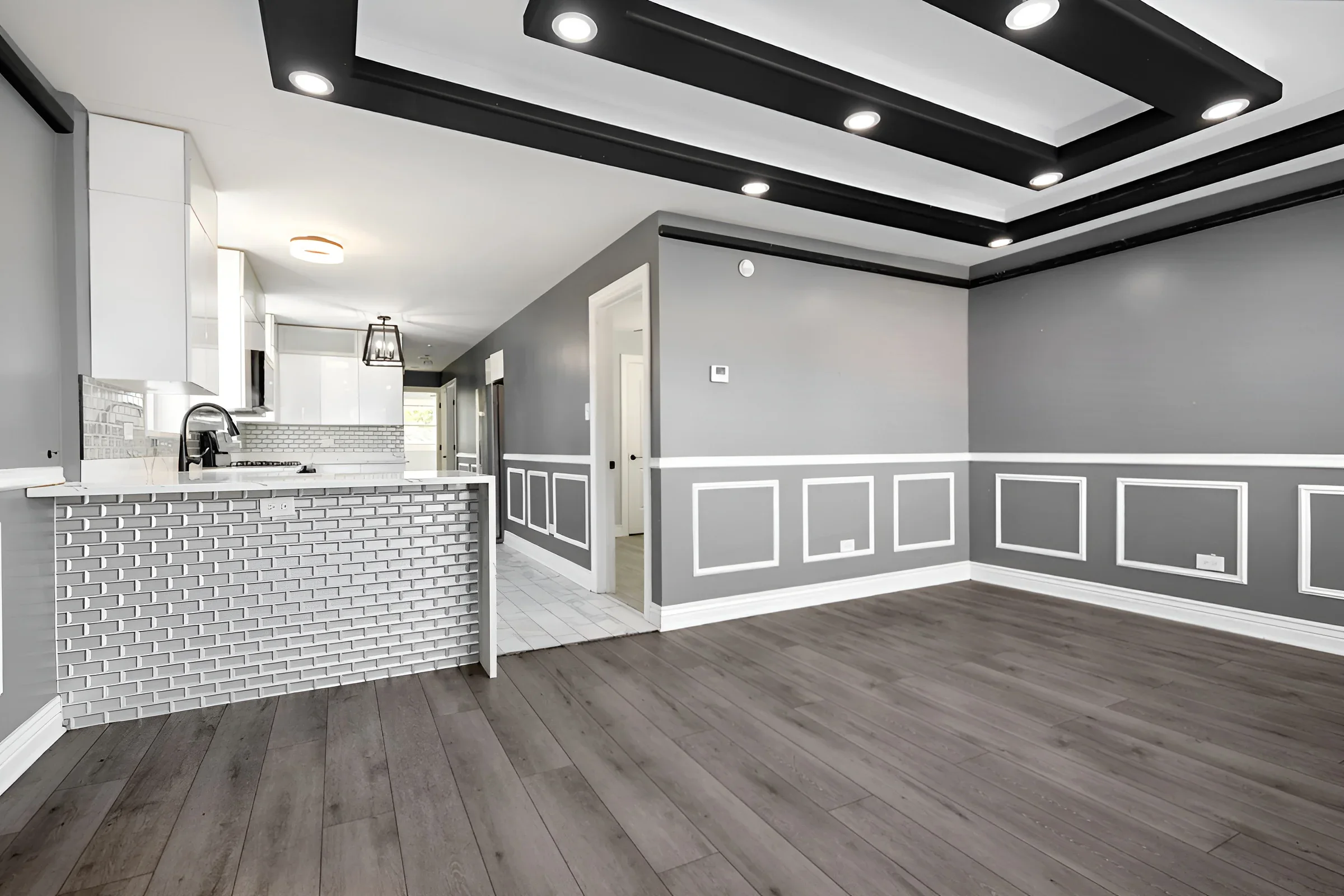 Dining room with picture-frame wainscoting and tray ceiling opening to the kitchen